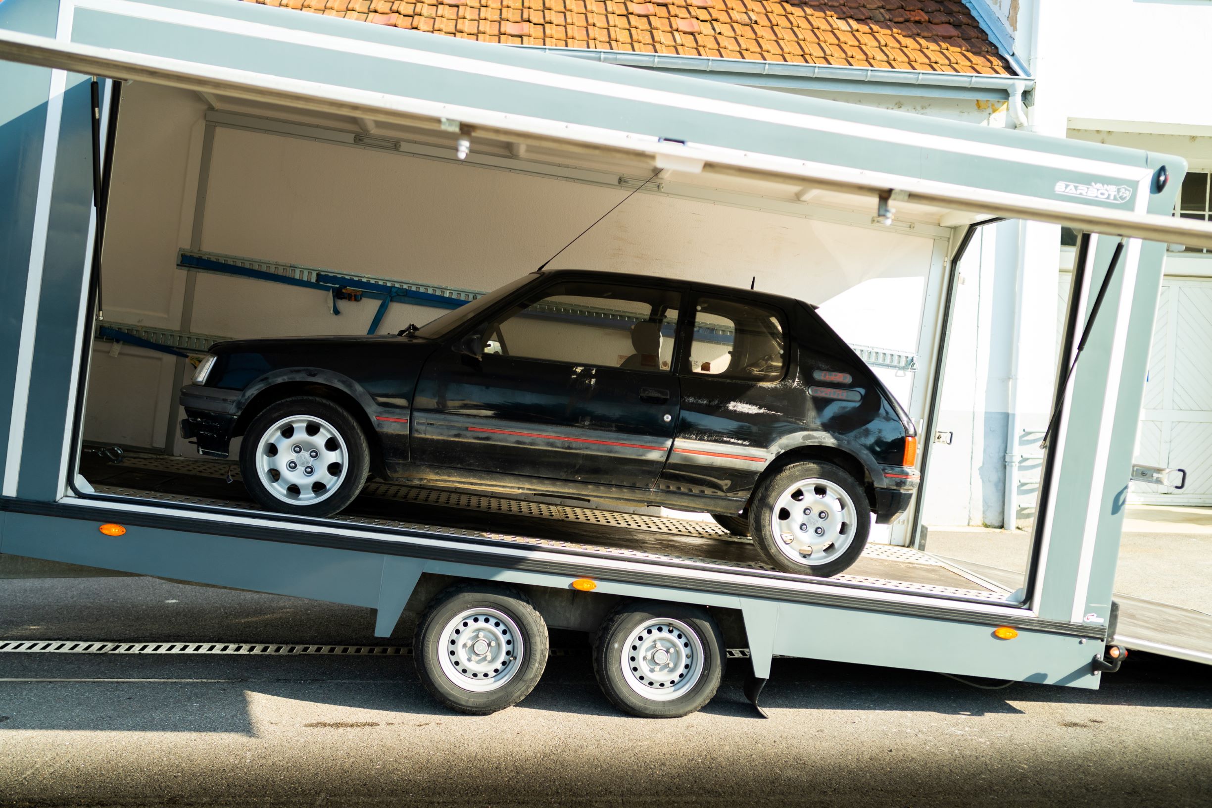 A black pre-restoration Peugeot 205 GTI in a trailer