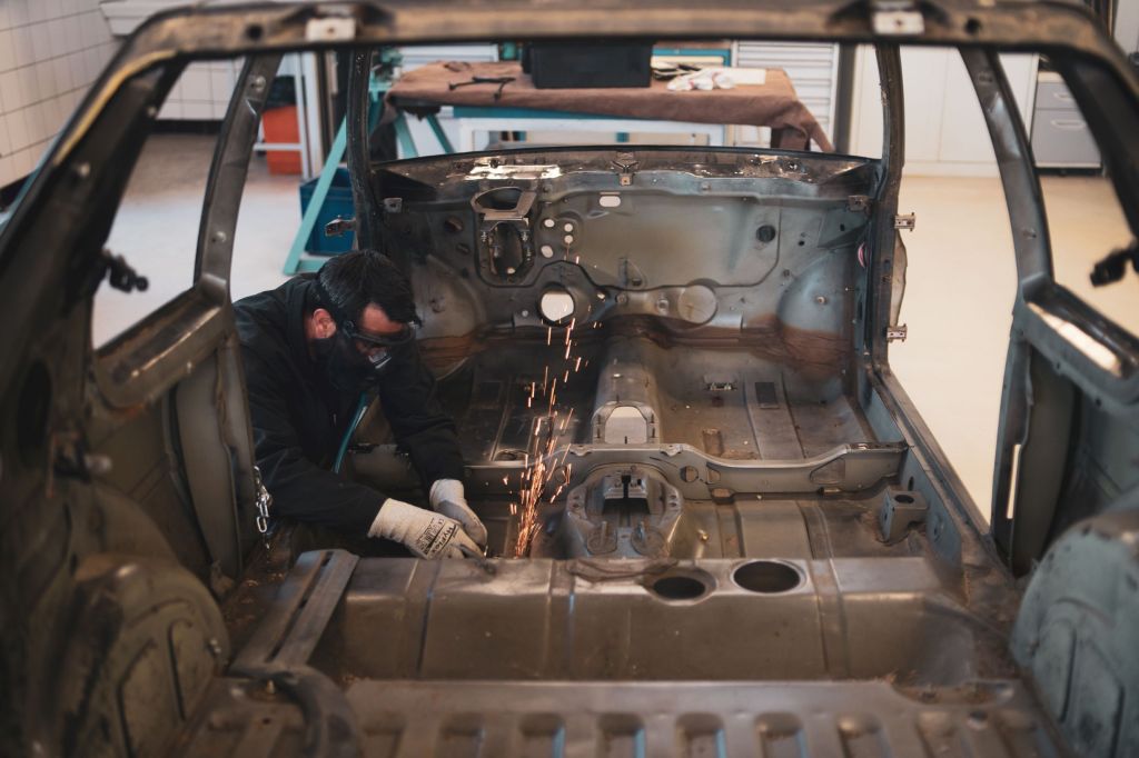 A restorer works on the bare-metal body of a Peugeot 205 GTI