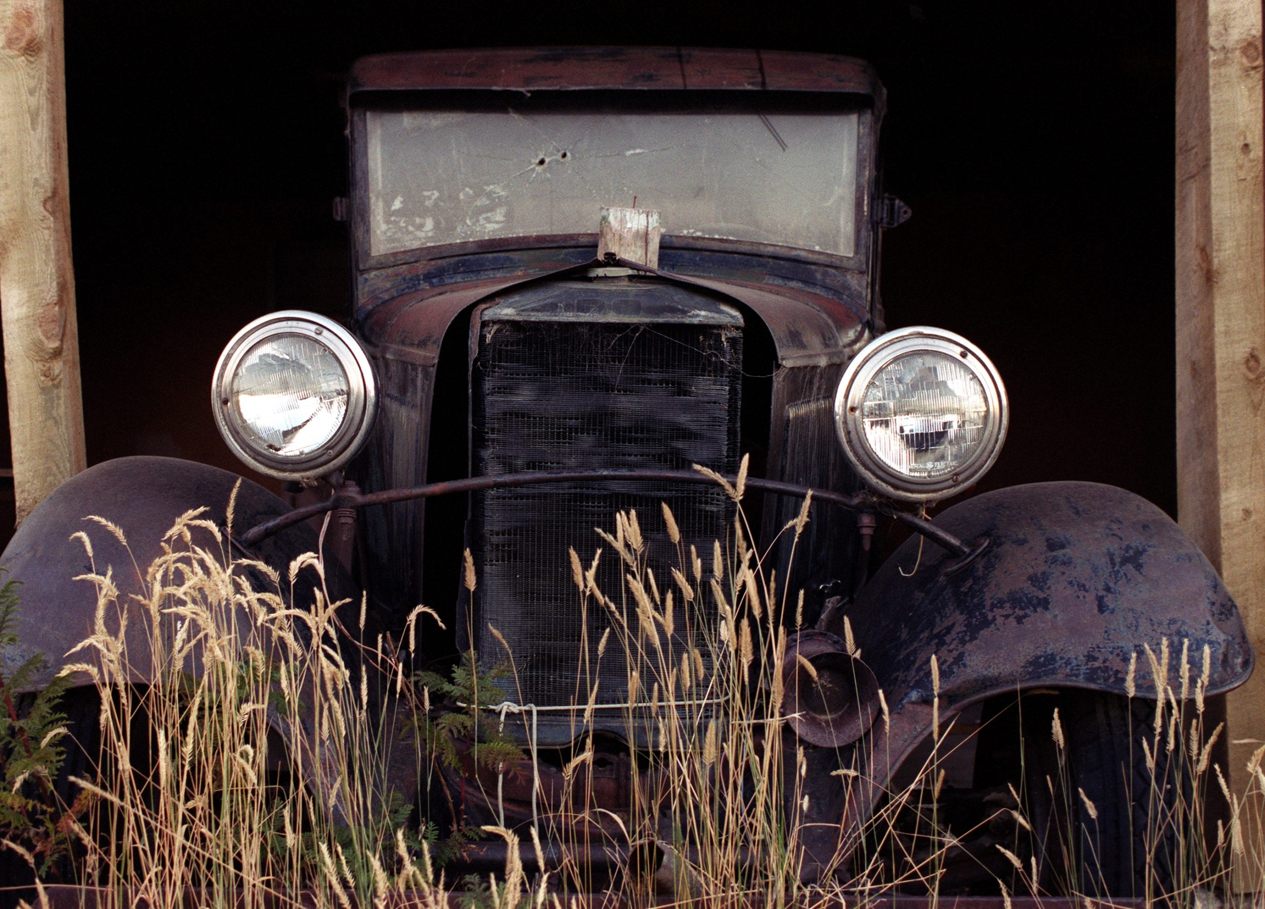 A rusty car sits in a barn waiting to be restored by somebody.