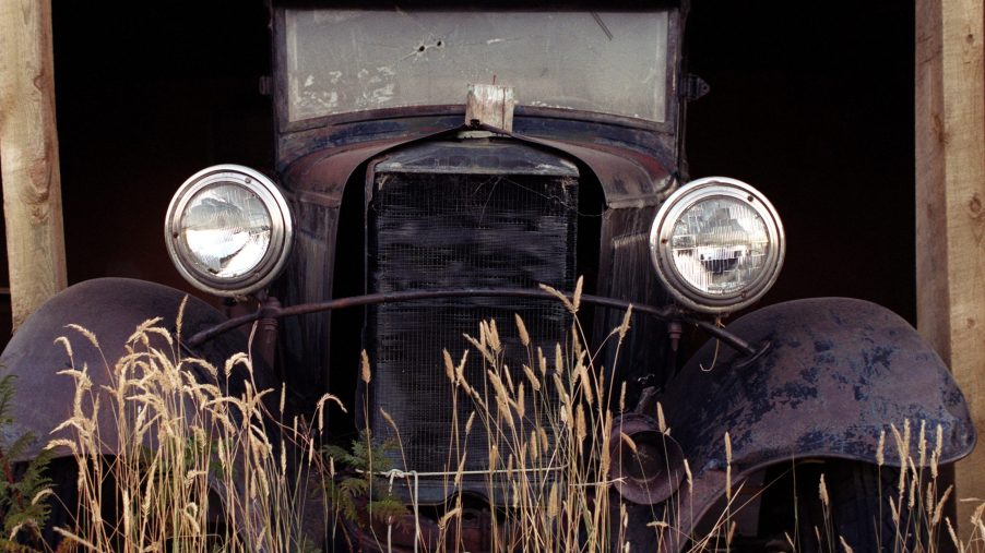 A rusty car sits in a barn waiting to be restored by somebody.
