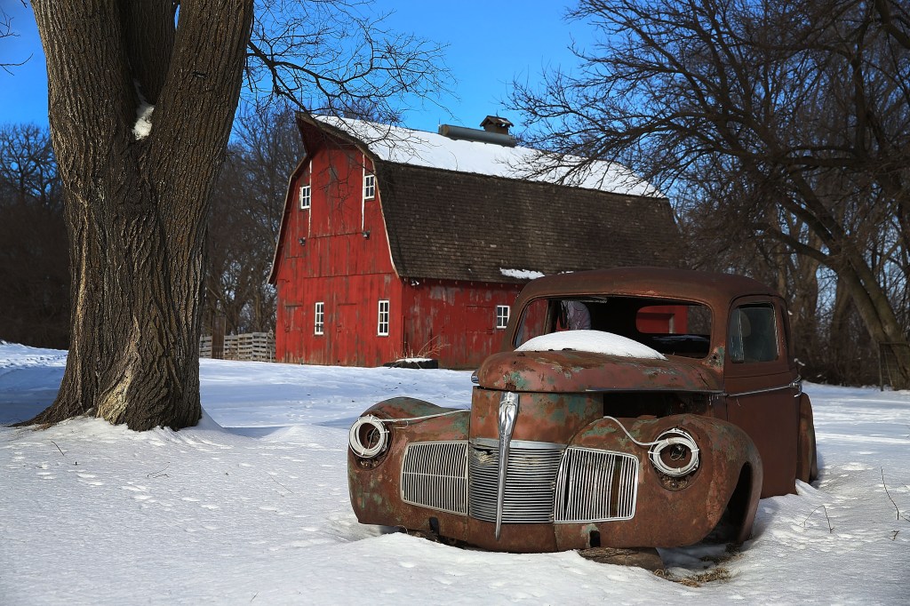 A rusty car in front of a barn in Iowa