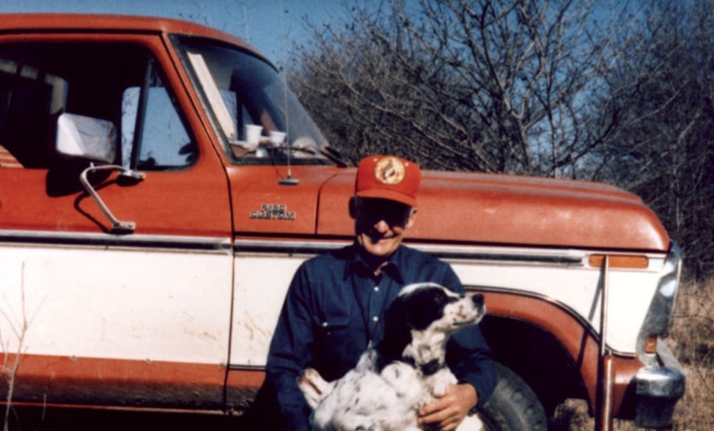 Sam Walton kneels in front of his red and white pickup to hug his dogs.