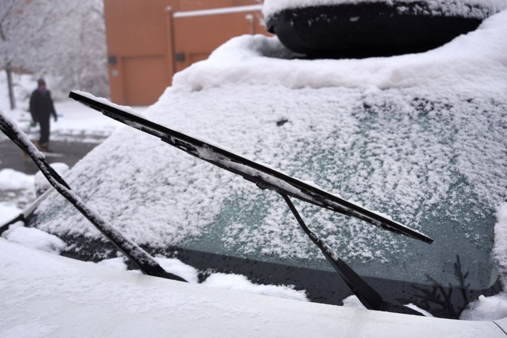 The windshield wipers and wiper blades of a snow-covered car