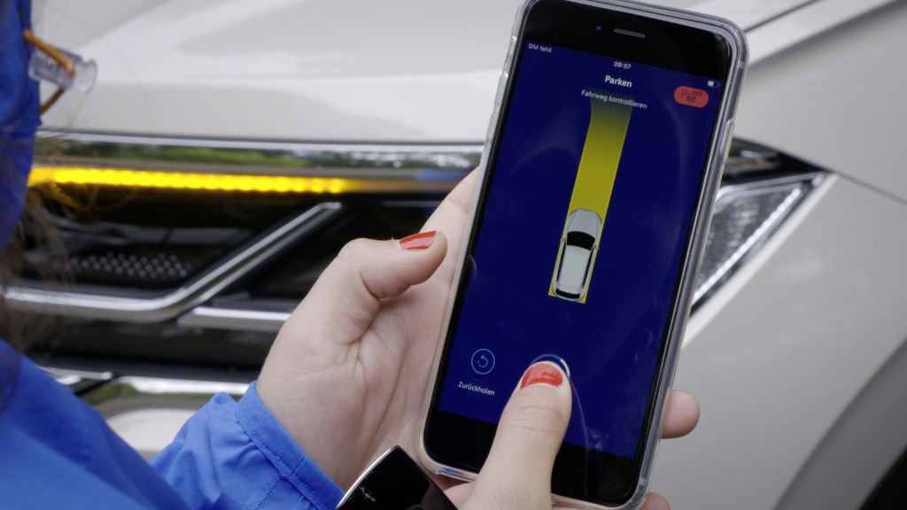 A woman using her smartphone to park her 2021 Volkswagen Touareg via park assist with remote control