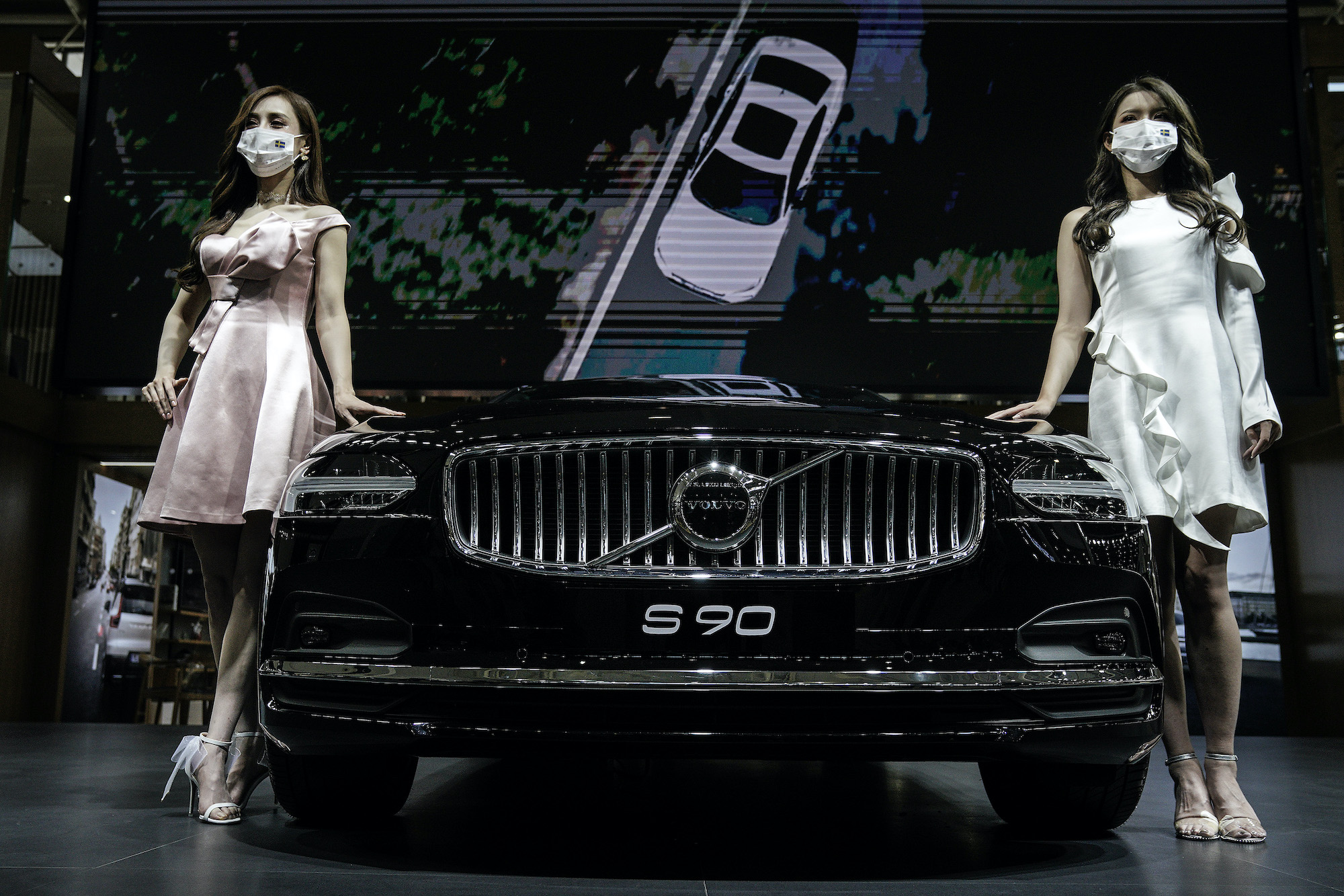 Models wear masks as a precaution while displaying a Volvo S90 in the Volvo stand during the 18th Central China International Auto Show