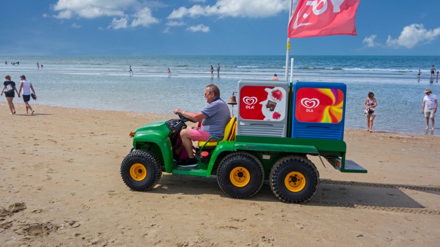 John Deere Gator transformed into ice-cream truck sells ice cream to tourists on the beach at a seaside resort on the North Sea coast.