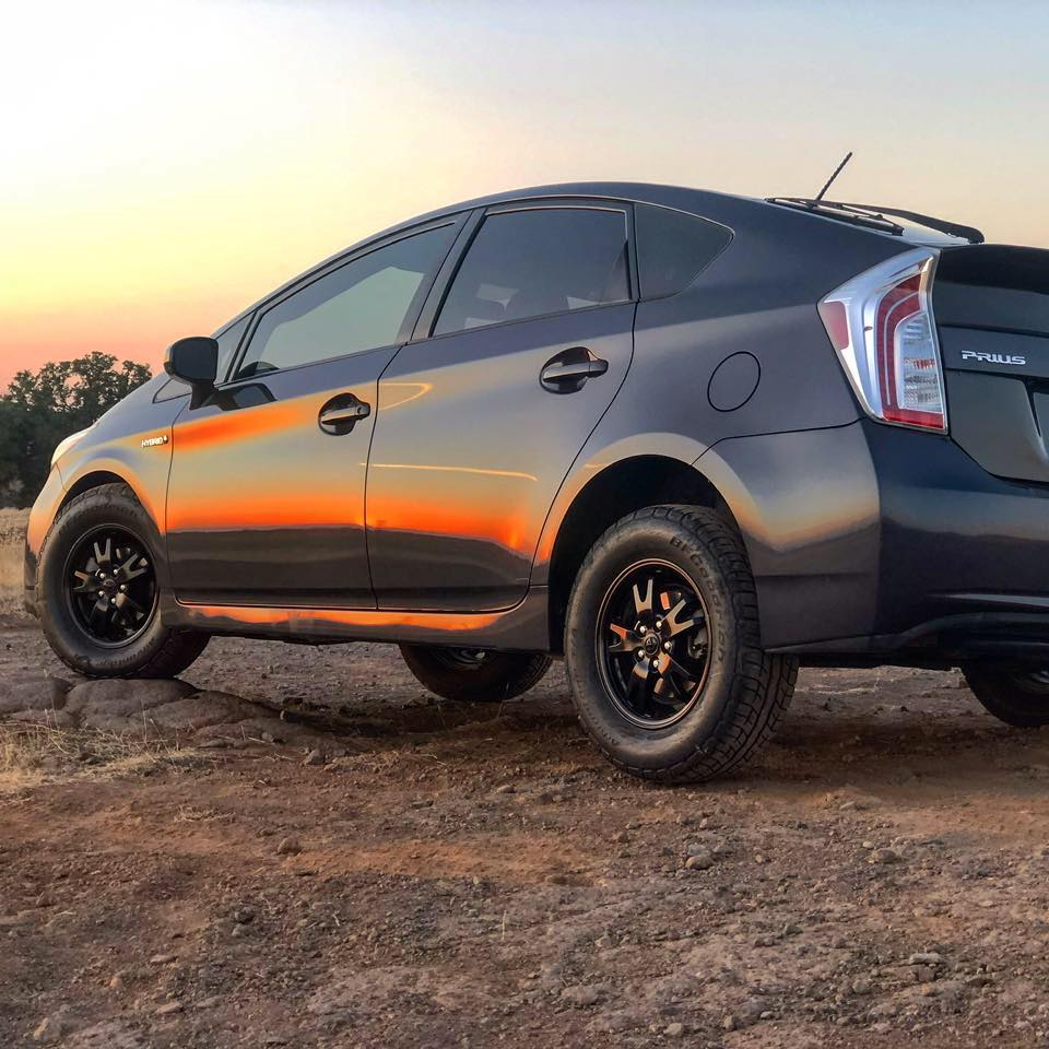 A black Toyota Prius with a lift kit sits on a dirt road.