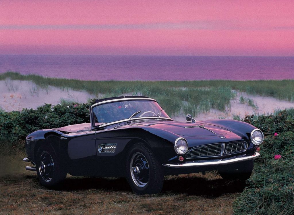 A black 1956 BMW 507 by a sunset pond