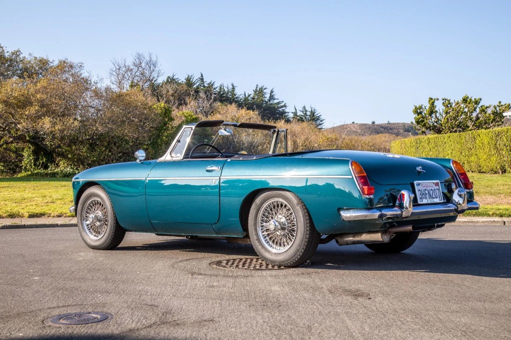 The rear 3/4 view of a turquoise 1965 MG MGB with its top down