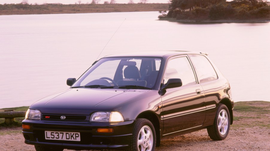 A dark-colored 1994 Daihatsu Charade GTI hatchback parked by a lake