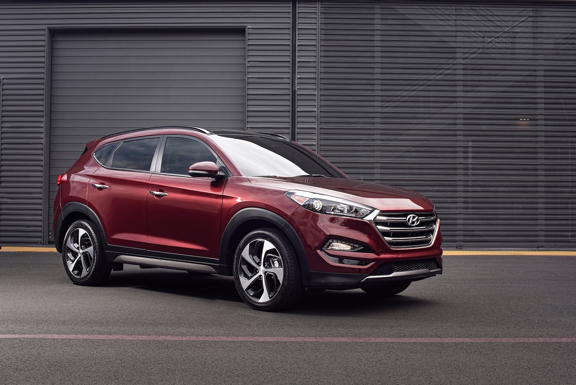 A dark-red 2016 Hyundai Tucson parked on pavement in front of a dark-gray building