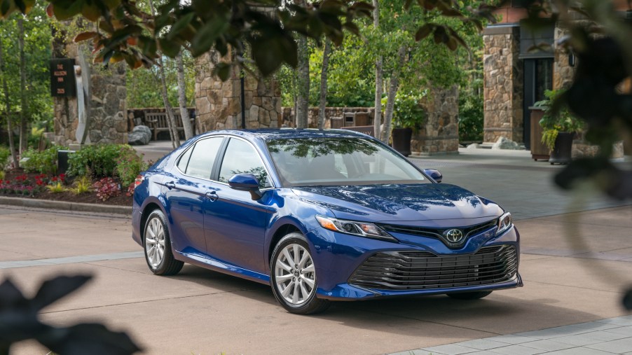 A blue 2018 Toyota Camry LE is parked in a driveway outside a home with landscaping.