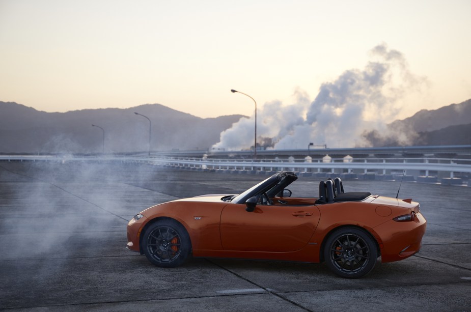 An orange Mazda Miata parked near the side of the road surrounded by smoke