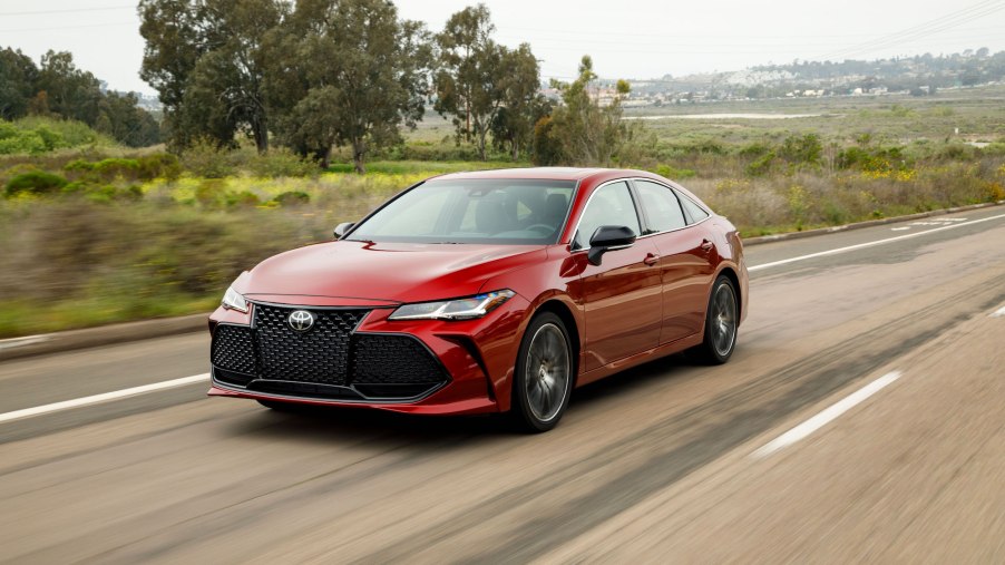 A red 2019 Toyota Avalon drives on a foliage-lined road outside a city.