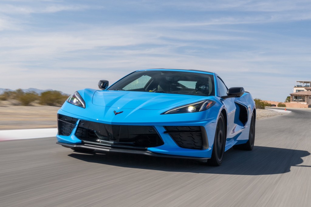 A Rapid Blue 2020 Chevy Corvette travels on a paved surface with an arid landscape, mountains, and a blue sky with wispy clouds in the background