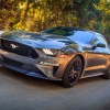 A dark-gray metallic Ford Mustang drives on a tree-lined road