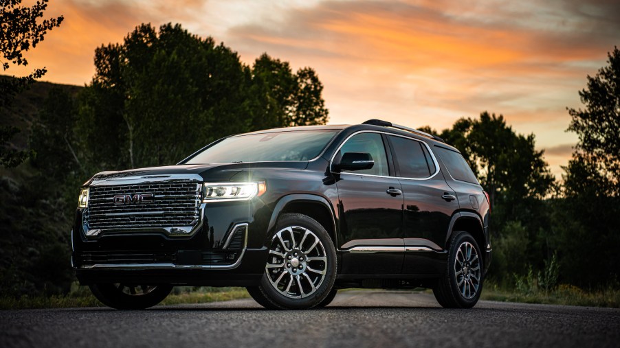 A black 2020 GMC Acadia Denali is parked on asphalt in front of trees and an orange sky