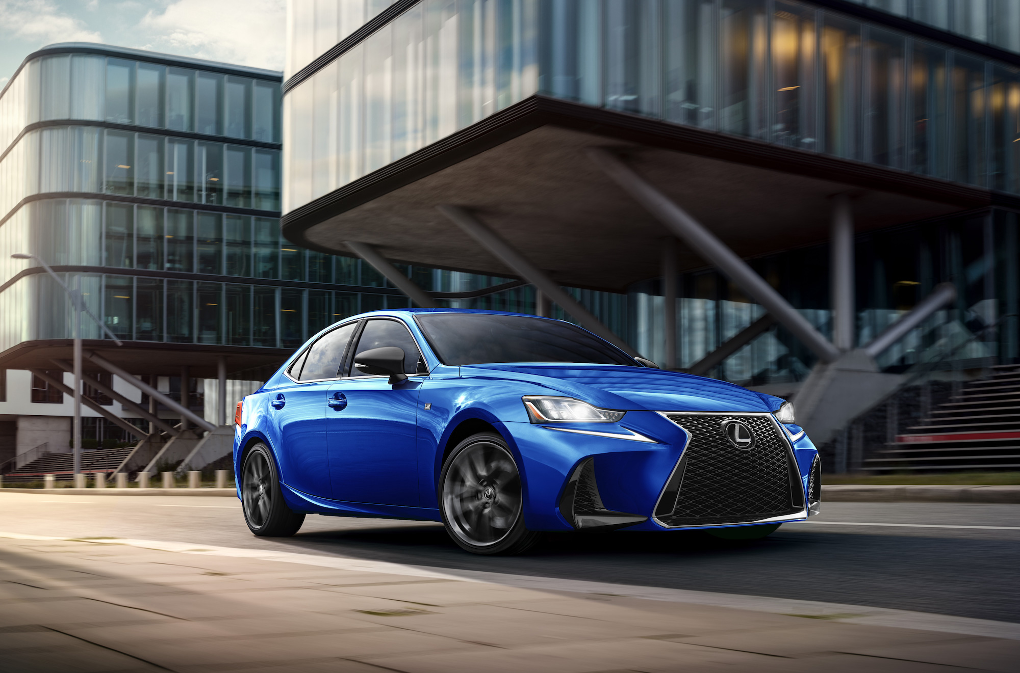 A blue 2020 Lexus IS sedan sits in front of two gray buildings.