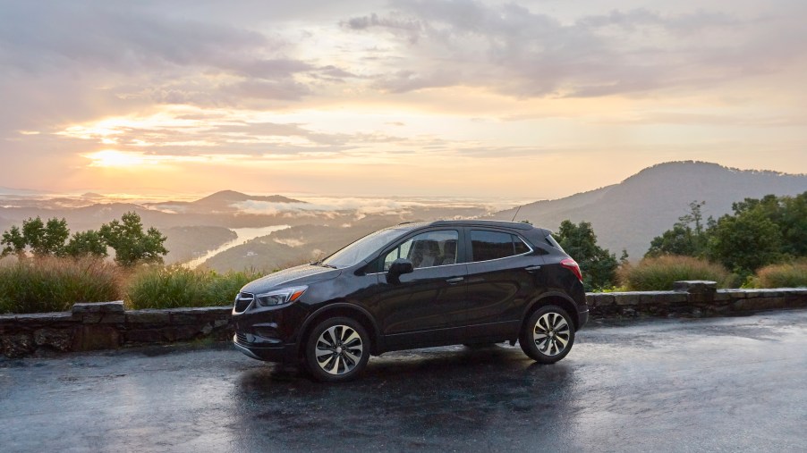 A 2021 Buick Encore sits parked on a wet paved road overlooking foliage and mountains