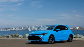 A sky-blue 2021 Toyota Corolla hatchback sits in front of a bay and cityscape