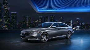 A silver 2021 Honda Accord Hybrid is parked on the roof of a building with a blue-lit overhang in front a nighttime cityscape in the background.