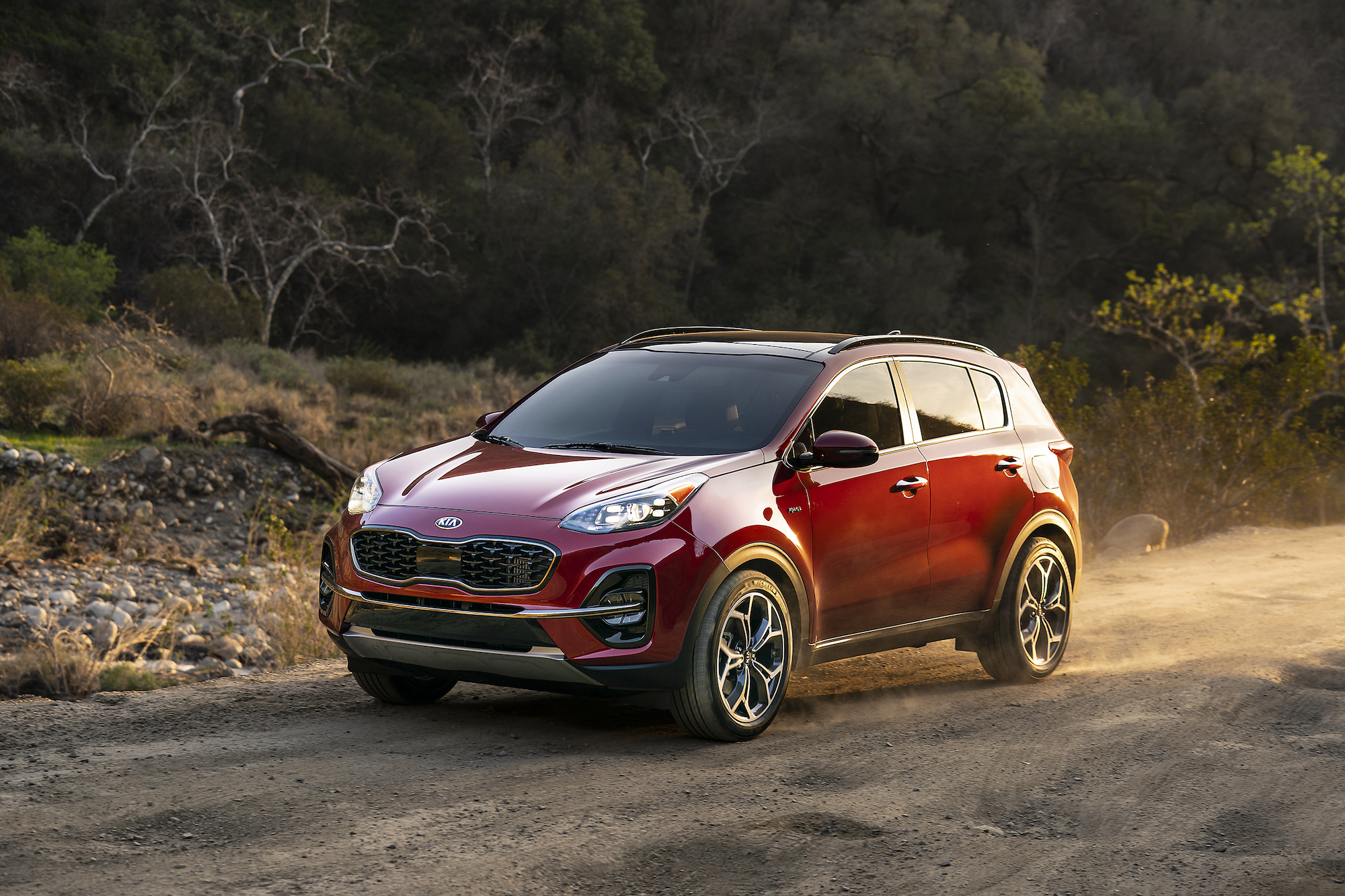 A dark-red 2021 Kia Sportage crossover SUV drives on a dusty road