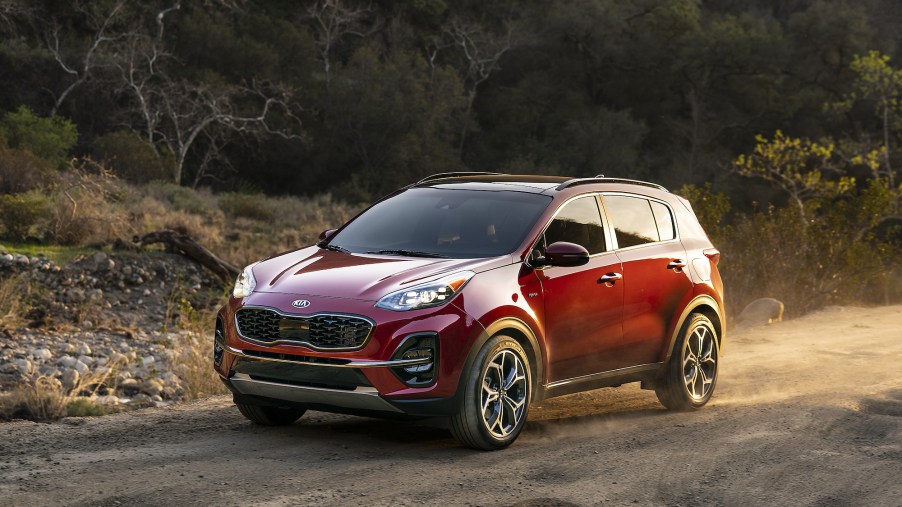 A dark-red 2021 Kia Sportage crossover SUV drives on a dusty road