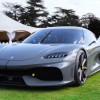A gray Koenigsegg Gemera supercar is parked on a green lawn with a white tent in the background.
