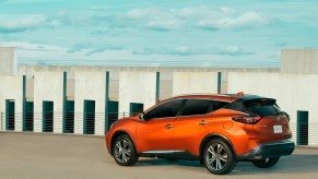 An orange 2021 Nissan Murano parked on display next to a wall with a blue sky in the background