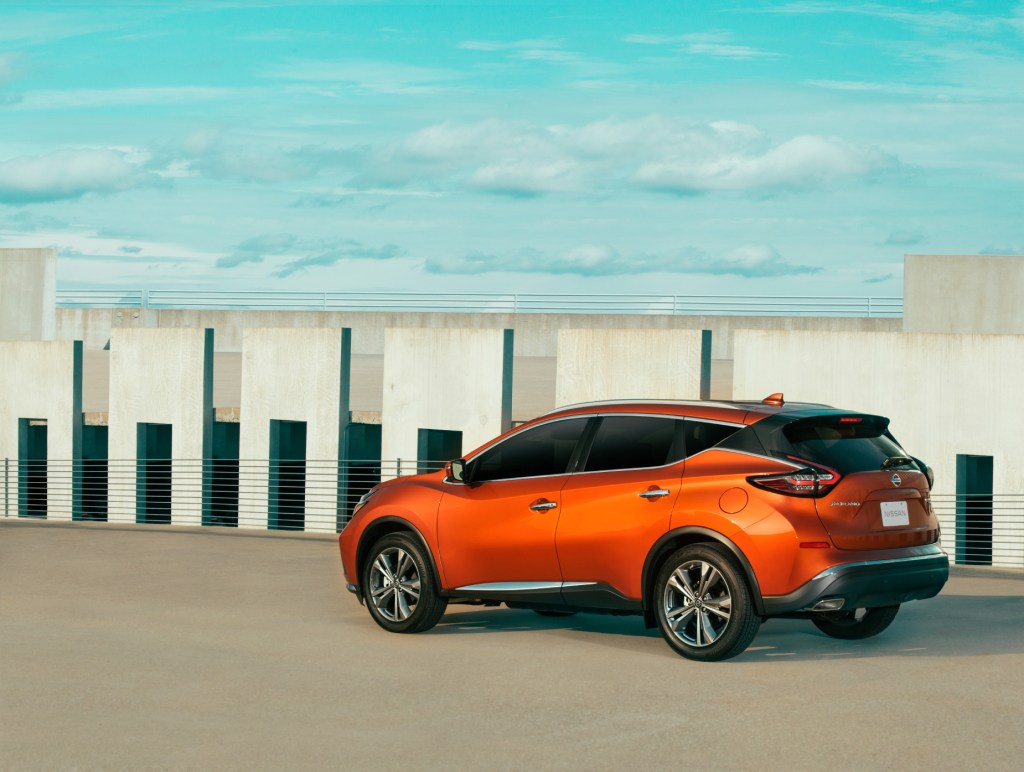 An orange 2021 Nissan Murano parked on display next to a wall with a blue sky in the background