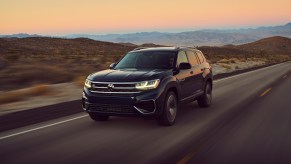 A black 2021 Volkswagen Atlas drives on a road with mountains in the background