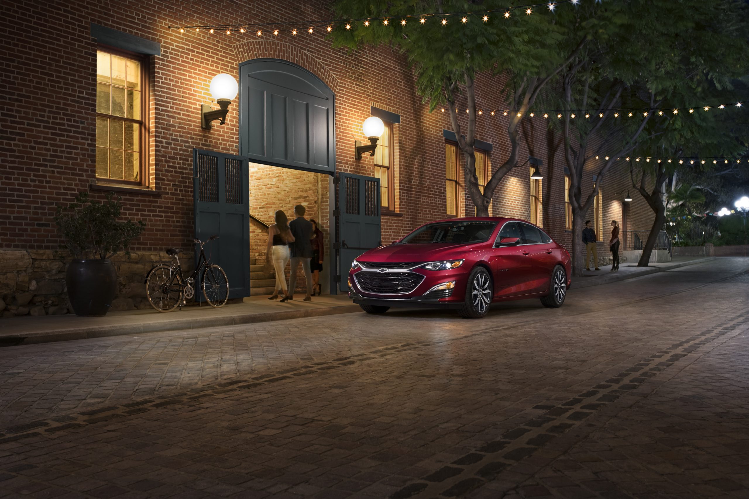 A red 2021 Chevy Malibu on display next to a building with lights on it