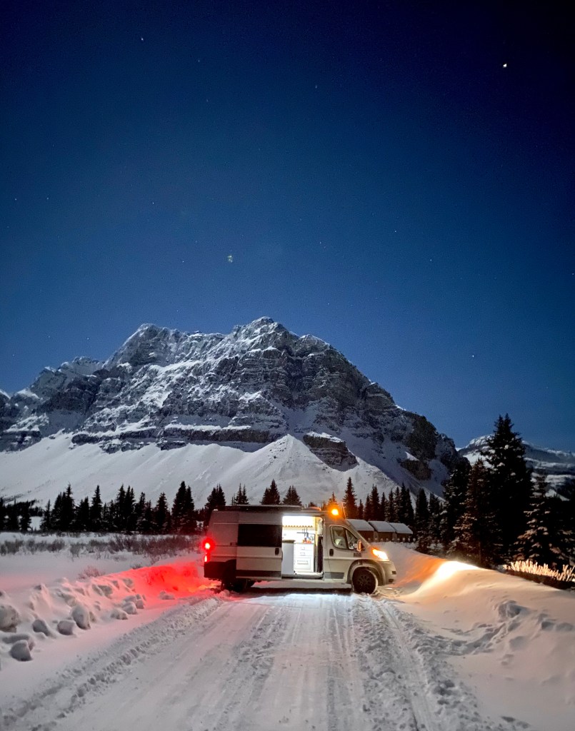 gorgeous night time photo of the camper van in the snow with a dusted mountain peak in the background