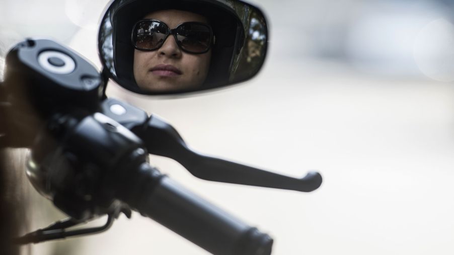A female motorcycle rider reflected in one of her Harley-Davidson mirrors