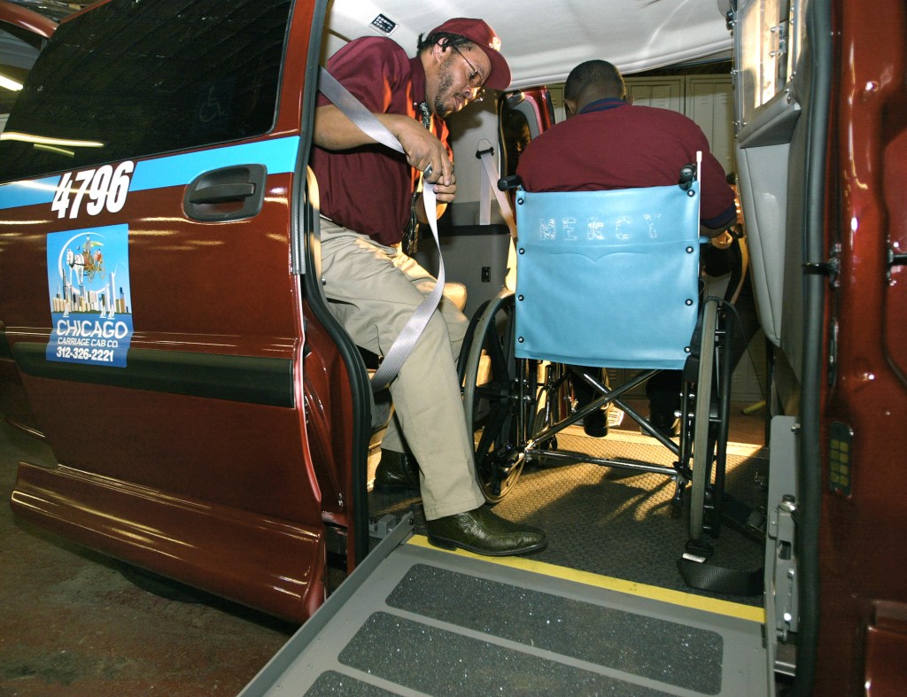 Chicago Carriage Cab taxi cab drivers William Bundy (L) and Rafiu Ayantoye use a ramp to load a wheelchair client