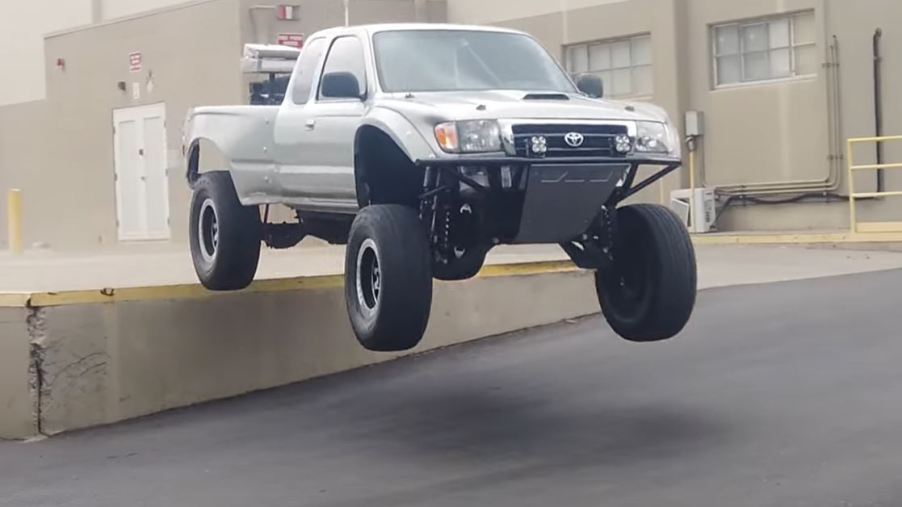 A Suxtom Silver Toyota Tacoma jumping off of an elevated loading dock.