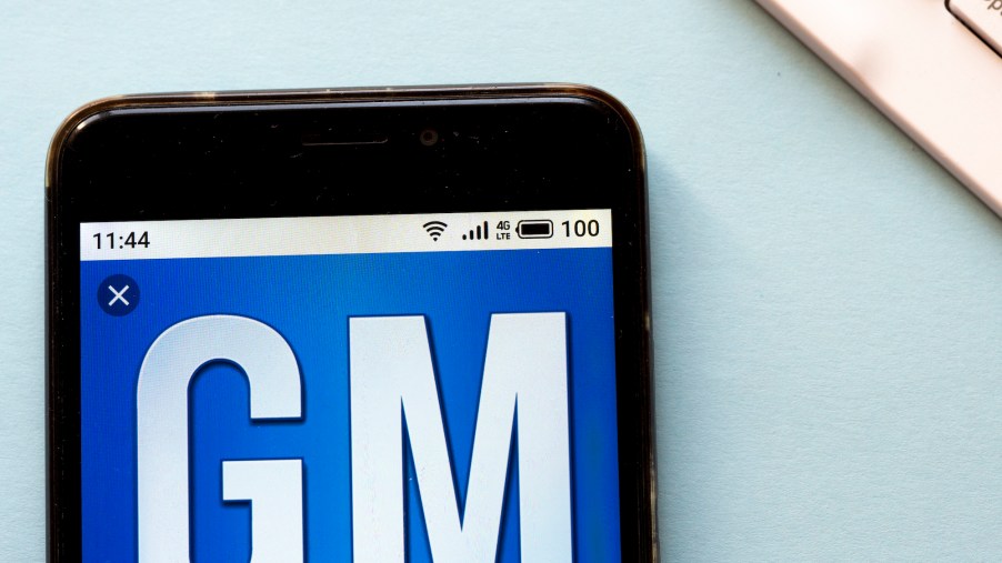 Photo illustration of a GM logo with a blue background and white letters shown on a cell phone's screen
