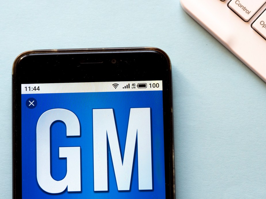 Photo illustration of a GM logo with a blue background and white letters shown on a cell phone's screen