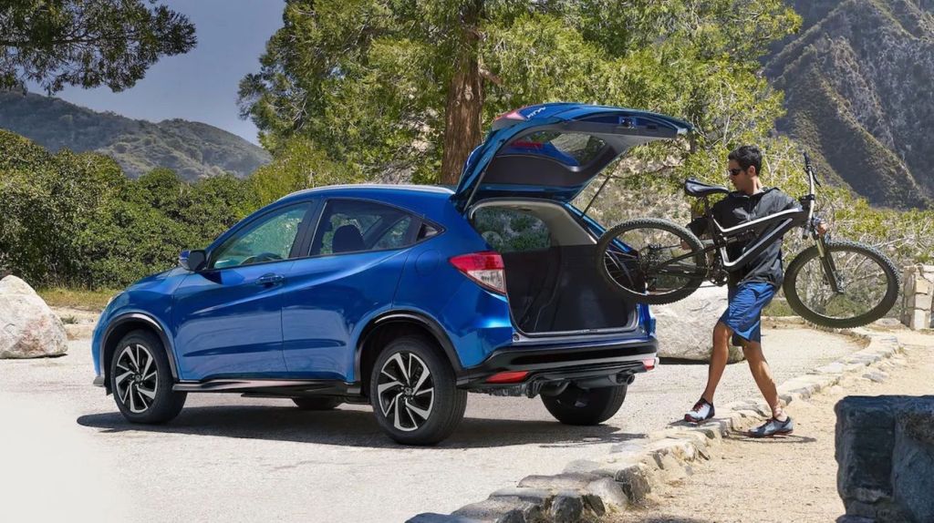 A man loading a bike into a blue 2021 Honda HR-V with the trunk open.