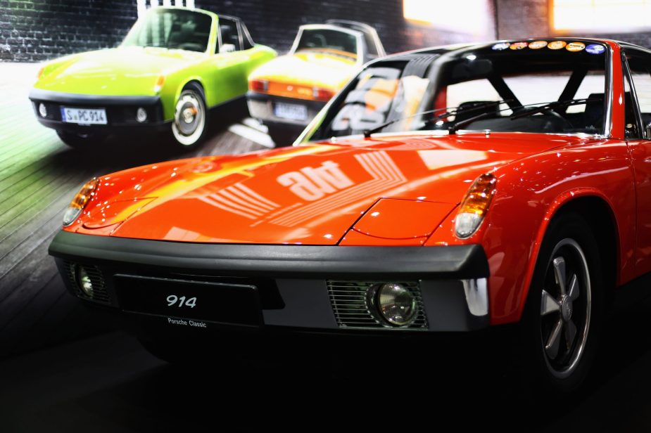 The front of a red Porsche 914 is in the foreground and a poster of another Porsche in the background.