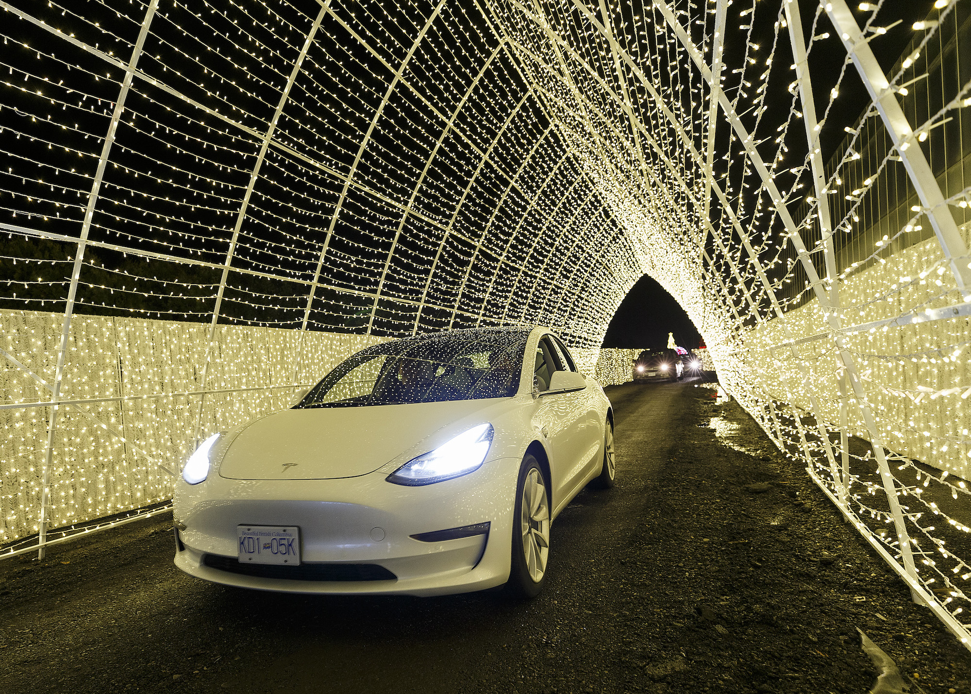 An electric vehicle passes through a Christmas light tunnel display at the Christmas Glow in Langley: Drive-Through Holiday Light Event at Milner Village Garden Centre on December 11, 2020, in Langley, British Columbia, Canada.