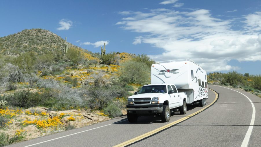 A pickup tows a fifth-wheel RV trailer around a bend in the road.