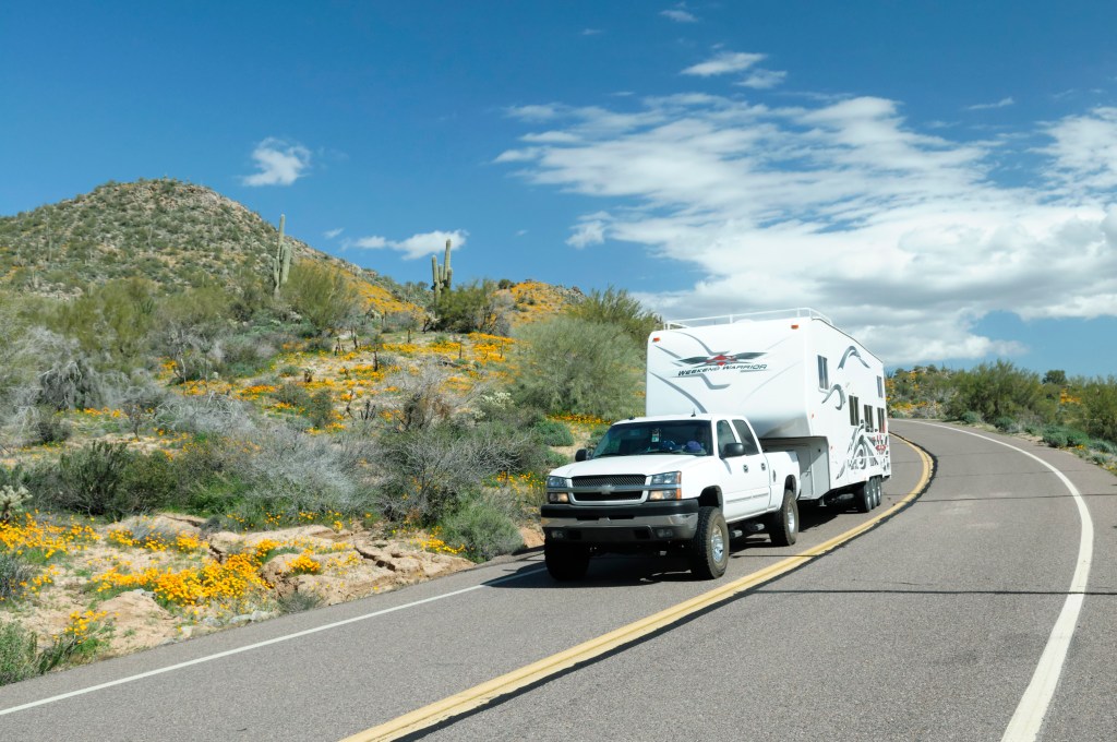 A pickup tows a fifth-wheel RV trailer around a bend in the road.