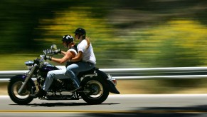 A motorcycle with two riders drives past wildflowers on the side of a road