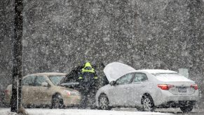 Two cars left straned in a winter storm as a man tries to help jump a car battery