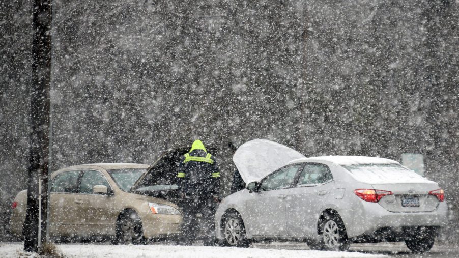 Two cars left straned in a winter storm as a man tries to help jump a car battery