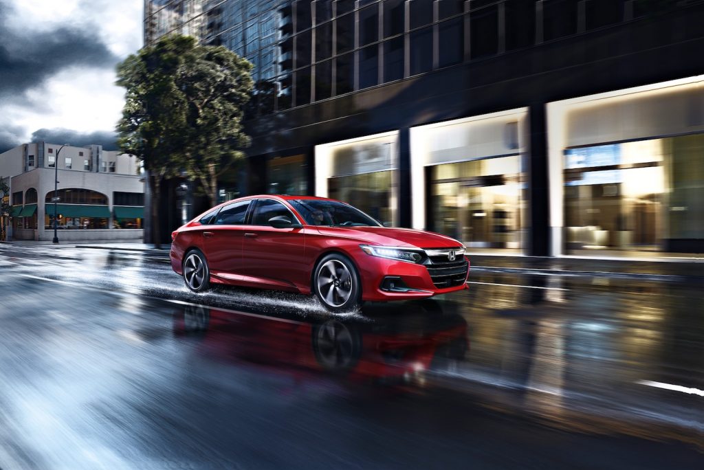 2021 Honda Accord Sport 2.0T sedan at speed in an urban area with stormy skies in the background