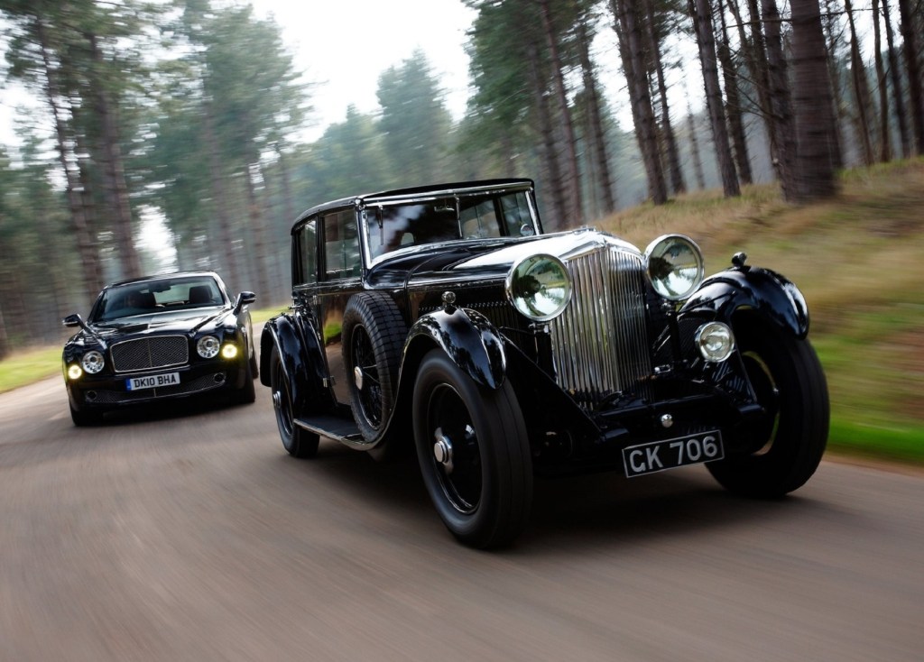 A black 1930 Bentley 8 Litre in front of a 2011 Bentley Mulsanne on a forest road