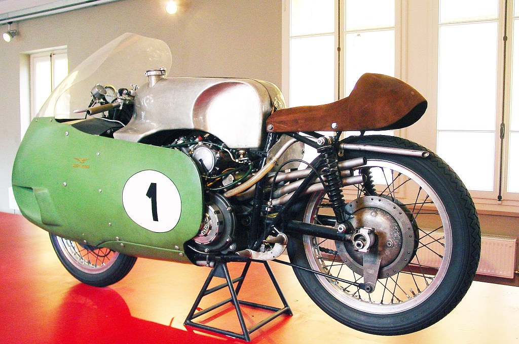 The rear 3/4 view of the silver-and-green 1955 Moto Guzzi V8 racer