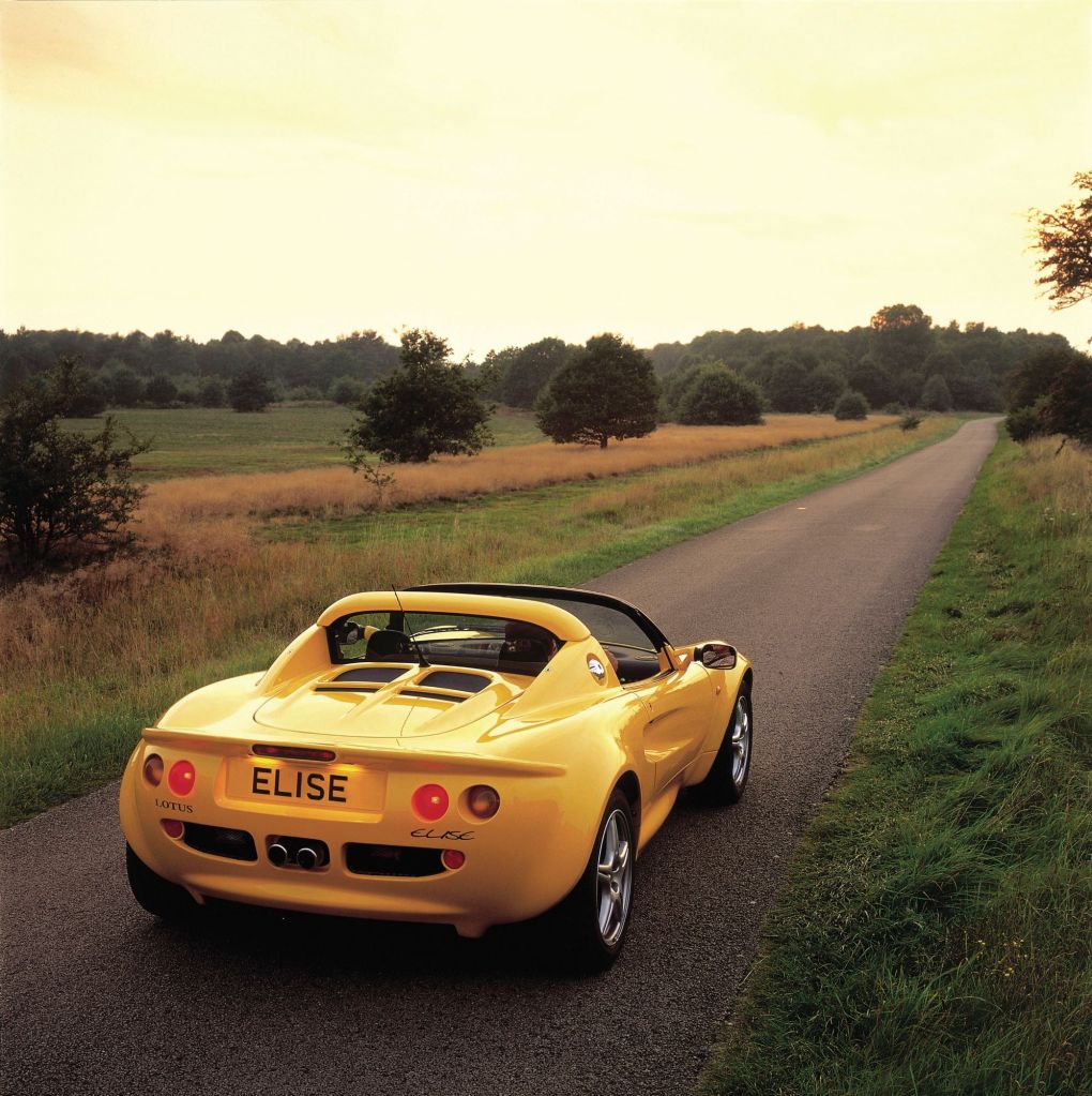 The rear view of a yellow 1996 Lotus Elise S1 on a country road